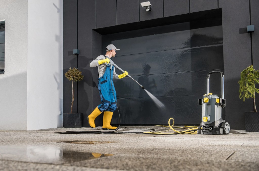 Worker in safety gear pressure washing a large commercial garage door